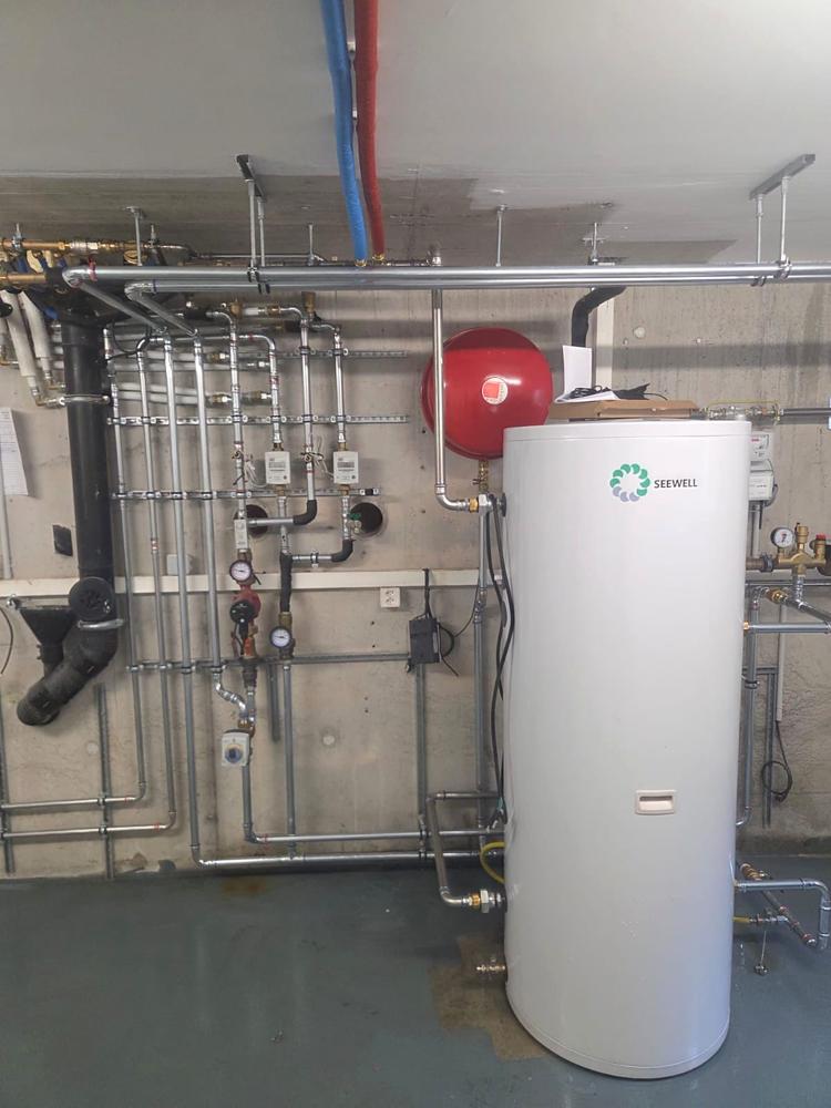 Chaufferie au sous-sol avec ballon Seewell, vase d'expansion et pompe de circulation, après le remplacement d'une chaudière à gaz par GRD à Lausanne