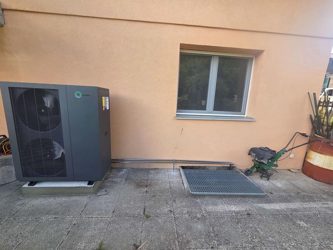 Unité extérieure d'une pompe à chaleur air-eau Seewell posée par GRD sur un socle contre une façade à Lausanne, avec ses liaisons jusqu'au saut-de-loup