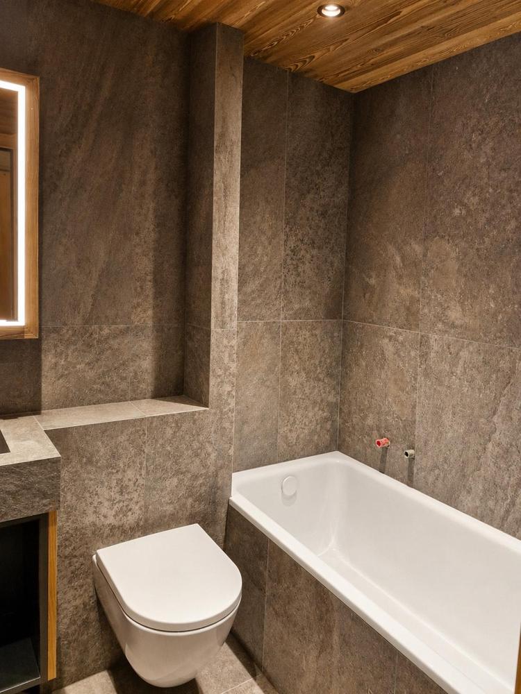 Salle de bain rénovée par GRD : carrelage pierre, plafond en bois, baignoire et WC suspendu