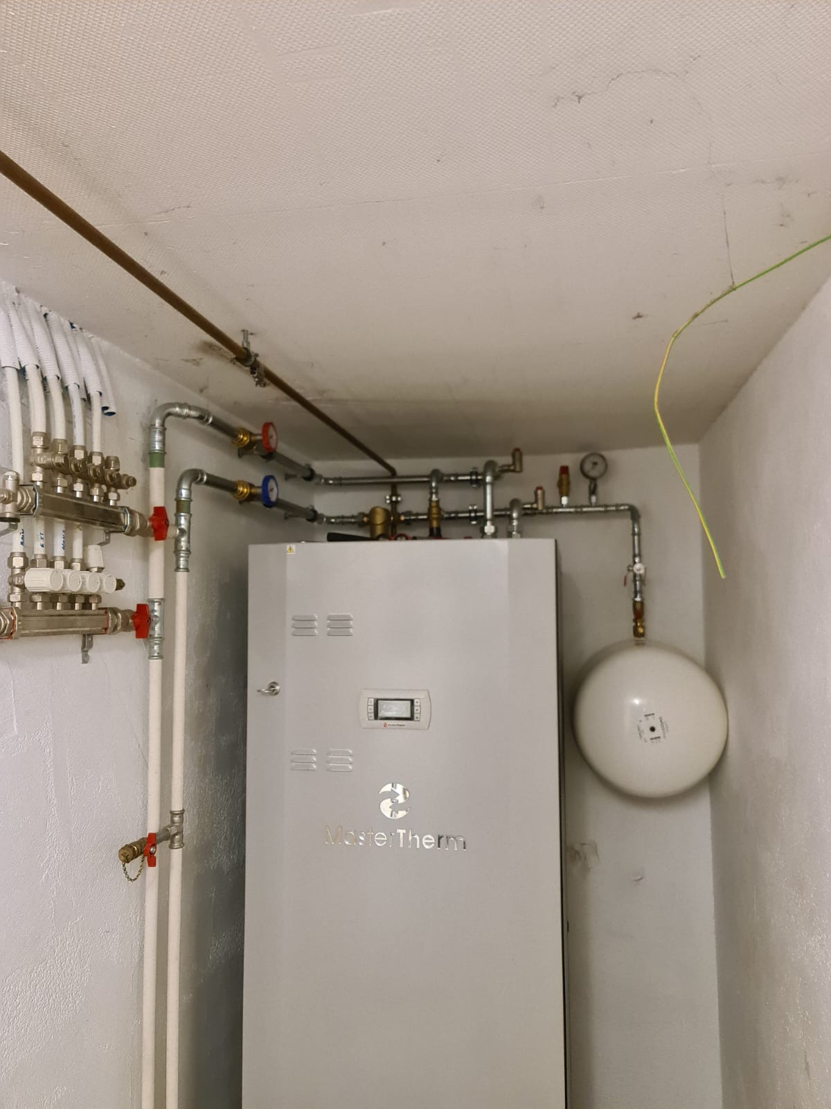 Pompe à chaleur installée par GRD dans un local technique, avec distribution et vase d'expansion